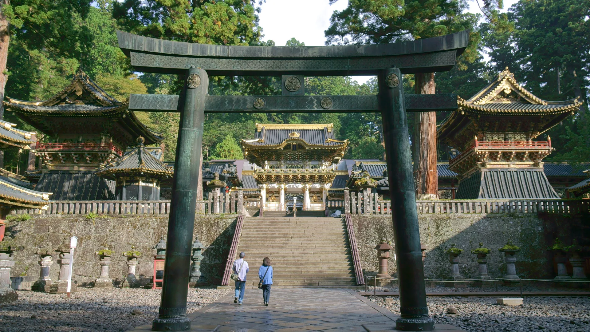 Kivinen torii-portti ja kultainen Yōmeimon-portti Nikko Tōshōgūn pyhäköllä, setripuiden lomasta katsottuna